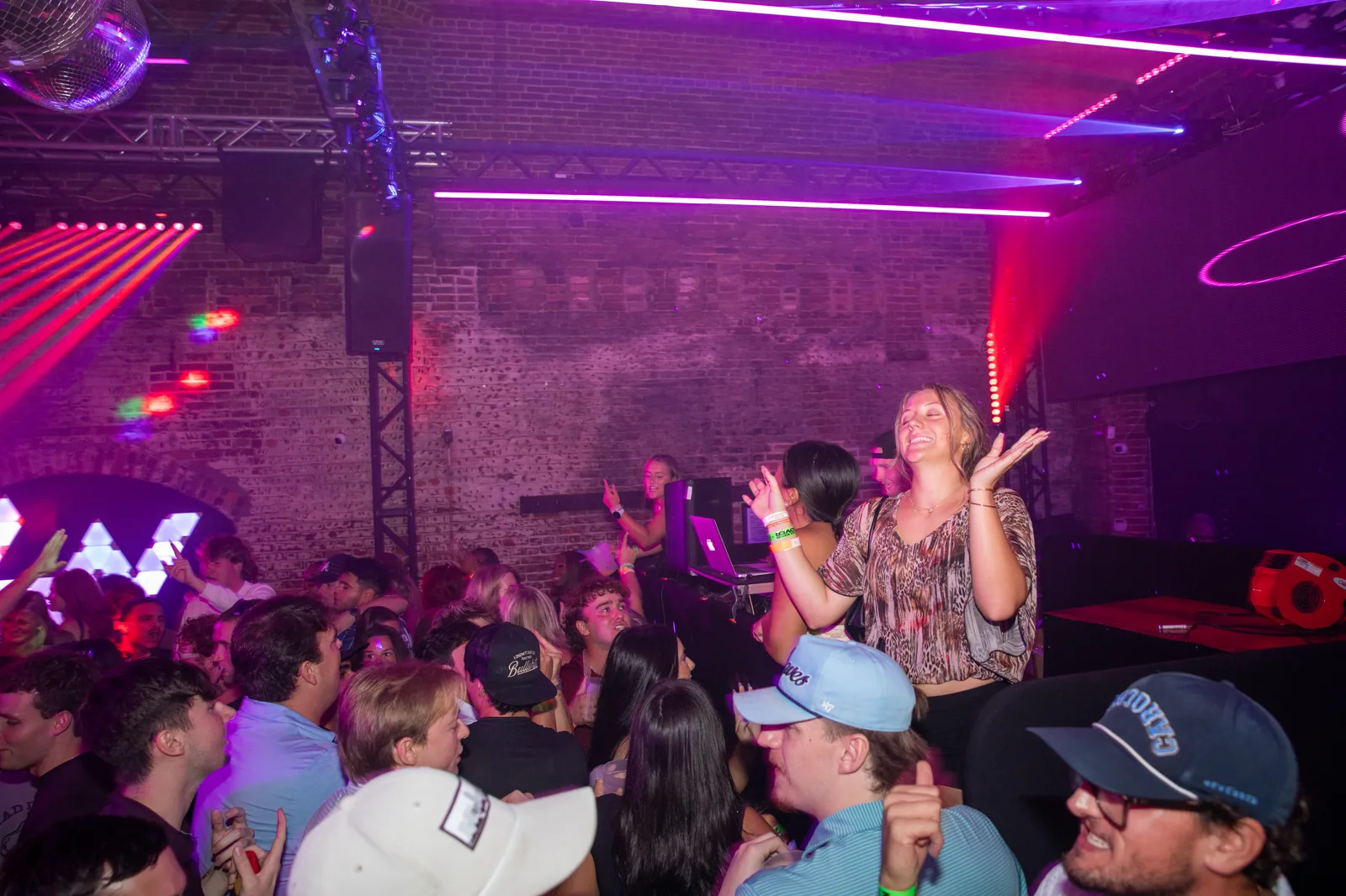Packed dance floor at Late Nite with hands in the air under magenta lighting